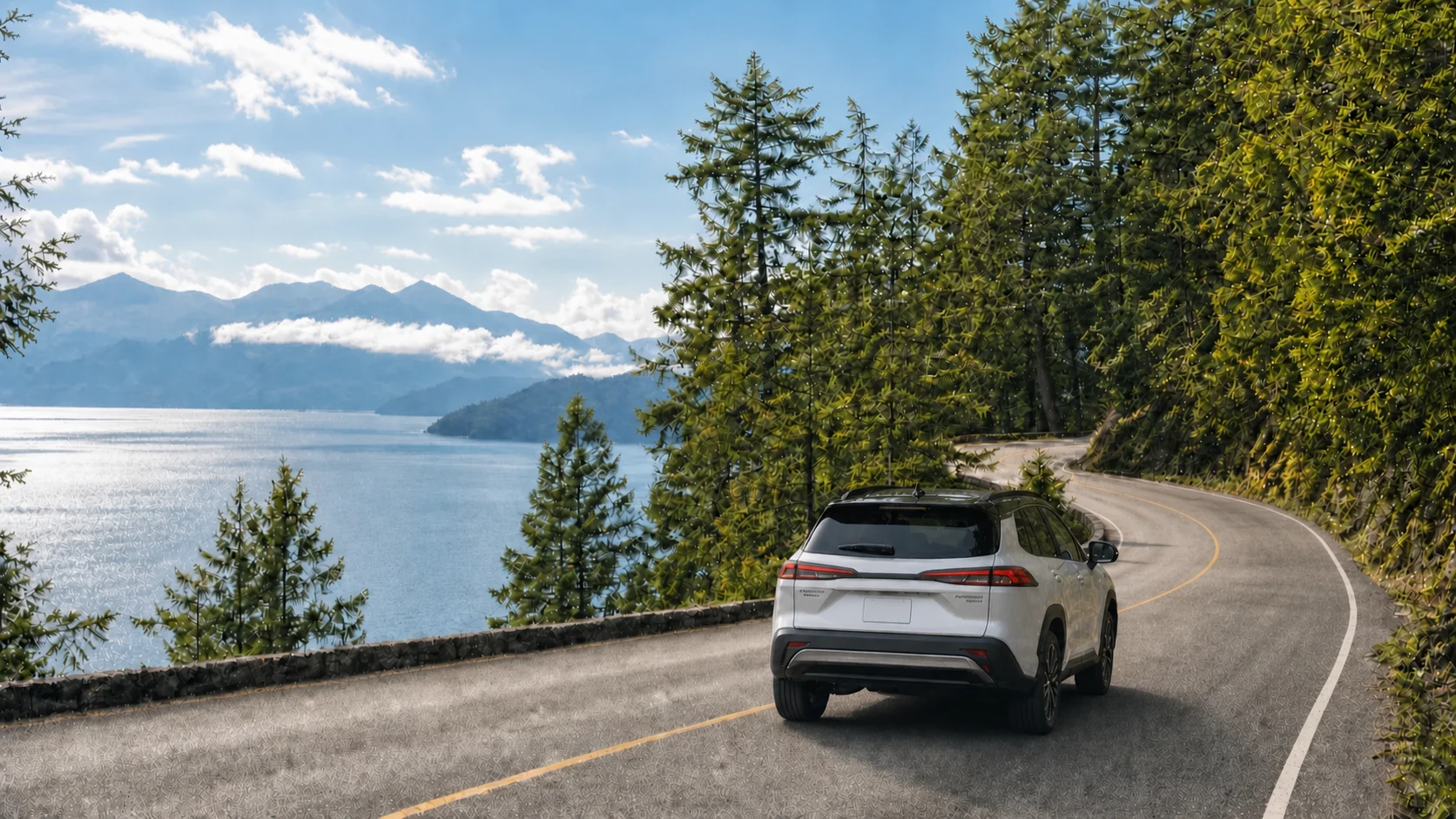 A silver 2026 Toyota Corolla Cross XSE Hybrid with a black roof travelling along a quiet North Shore road beside the water